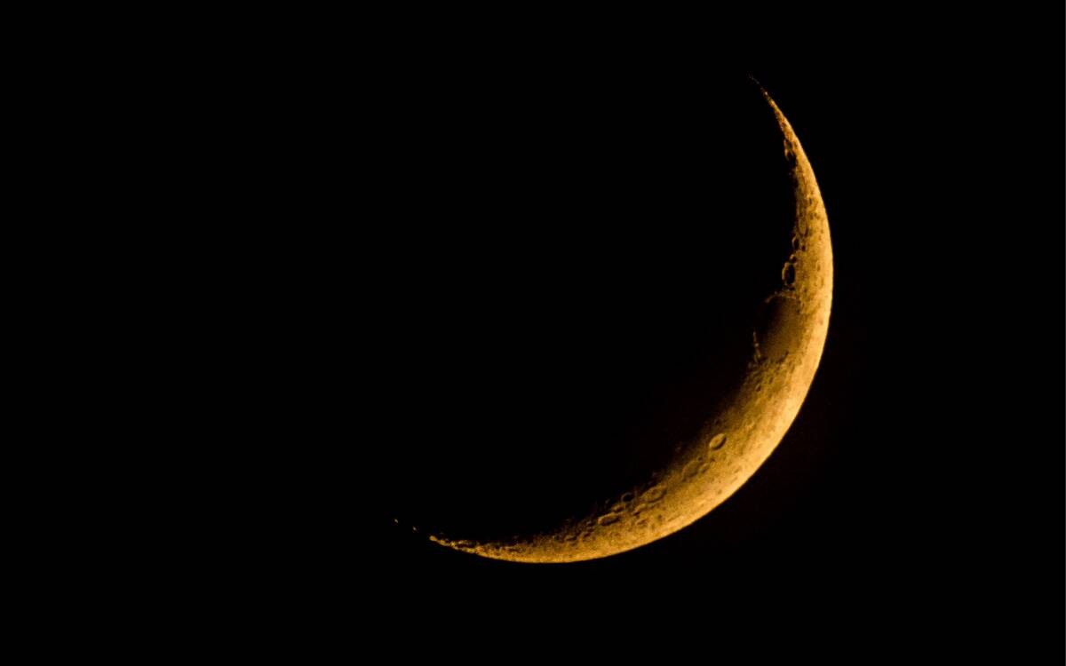 A yellow crescent moon hanging in a dark sky.