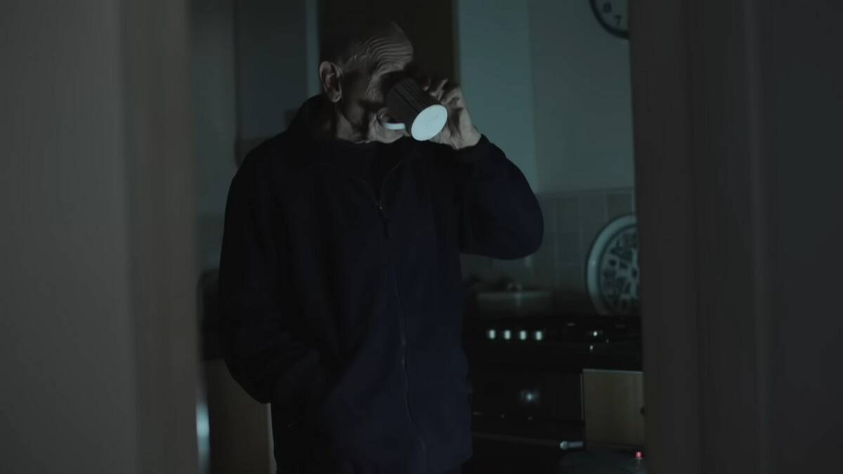 John having a mug of coffee in the dark, lit by a flashlight.