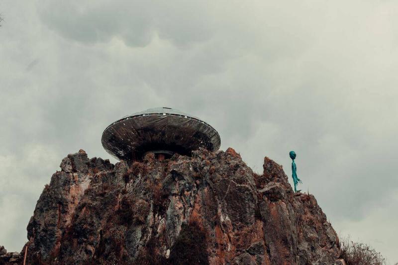 A UFO on a cliff, an alien statue poised next to it.