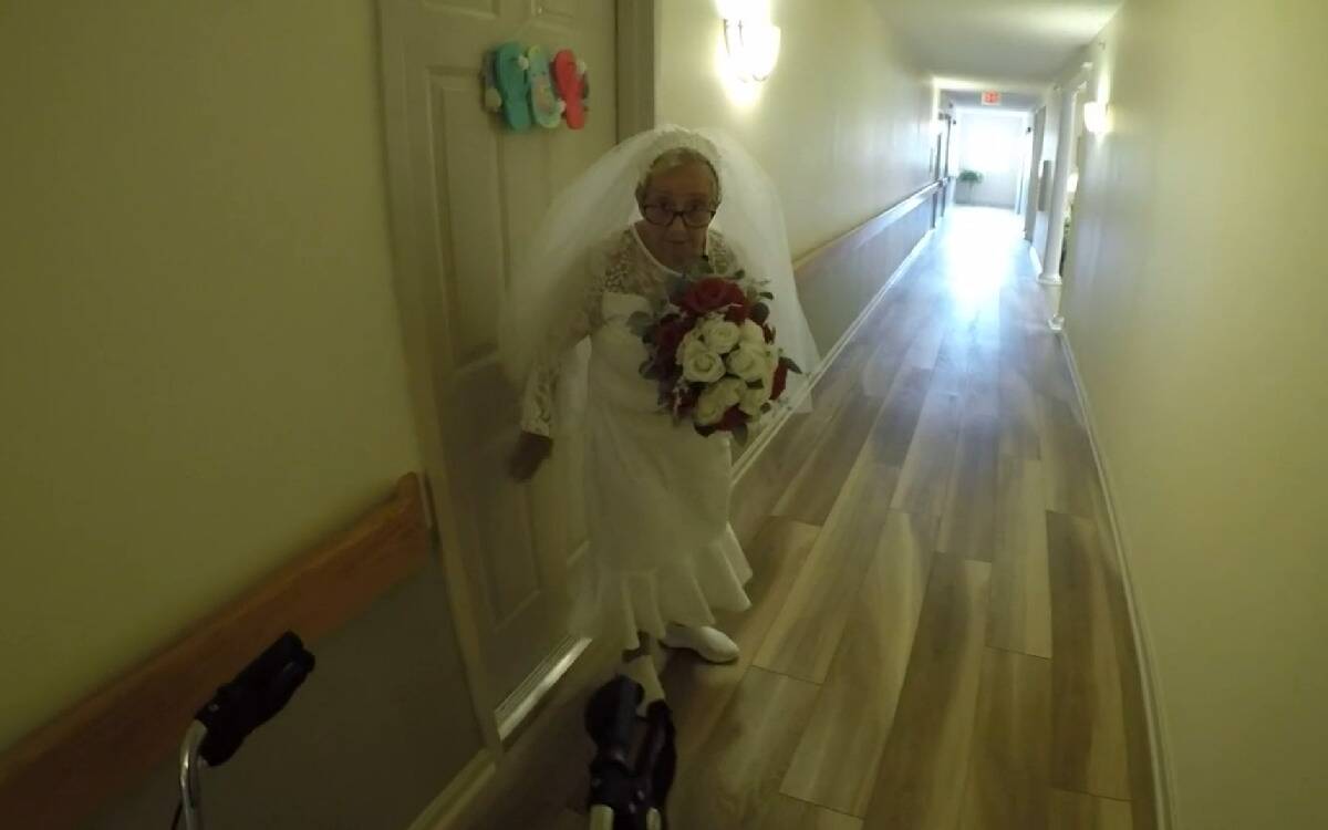 Fideli in her wedding dress on the day of the ceremony, holding her bouquet as she stands in the hallway outside her room.