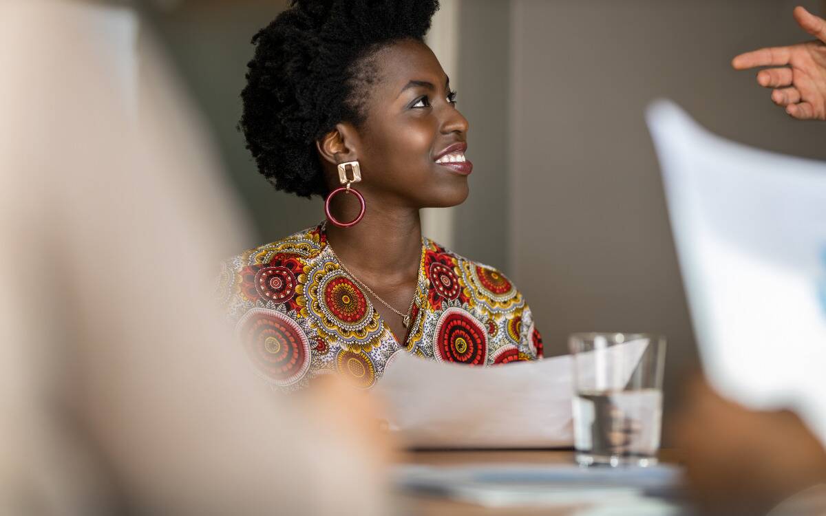 A woman seated at a meeting, listening intently as she smiles.