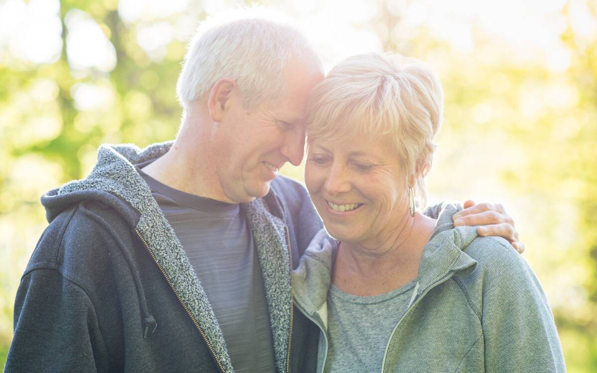 A mature couple walking outside, the man putting his arm around the woman and resting his forehead against her temple.