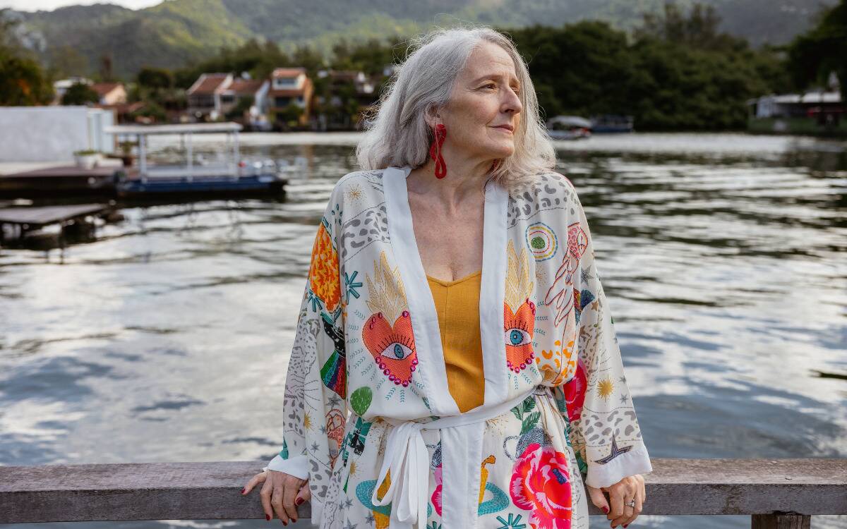 A woman in a colorful cardigan leaning against a railing in front of water.