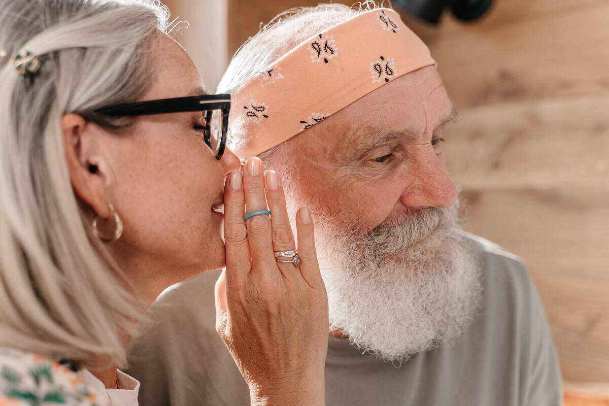 An older couple, one whispering into the other's ear.