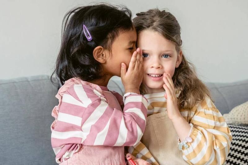 Two young girls, one whispering in the other's ear.