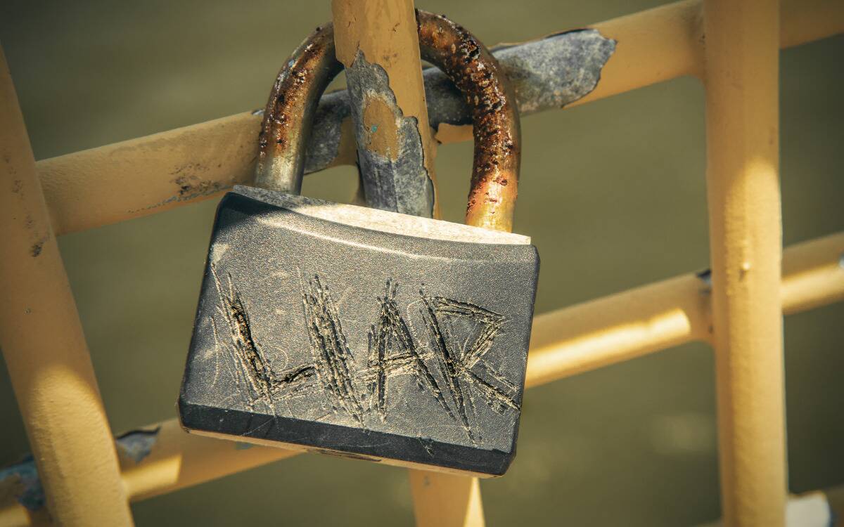 A lock on a fence with the word 'LIAR' crudely scratched in it.