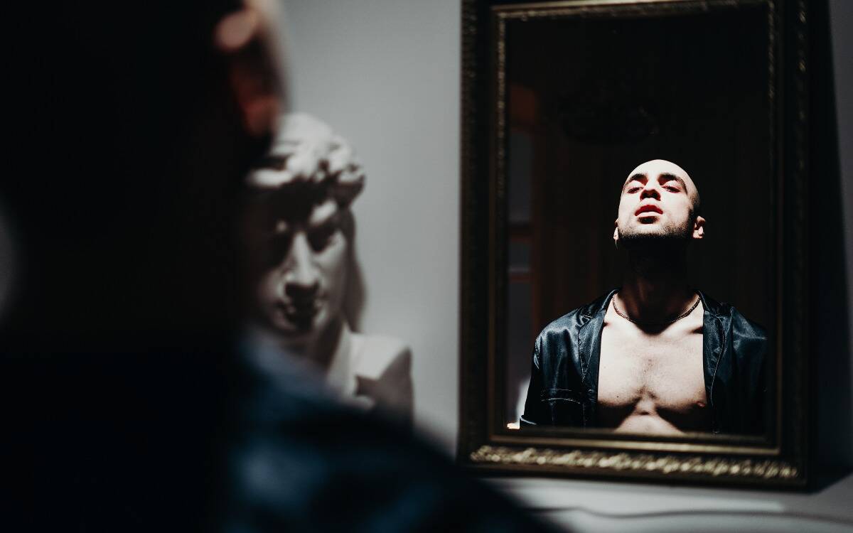 A man admiring himself in a mirror with dramatic lighting.