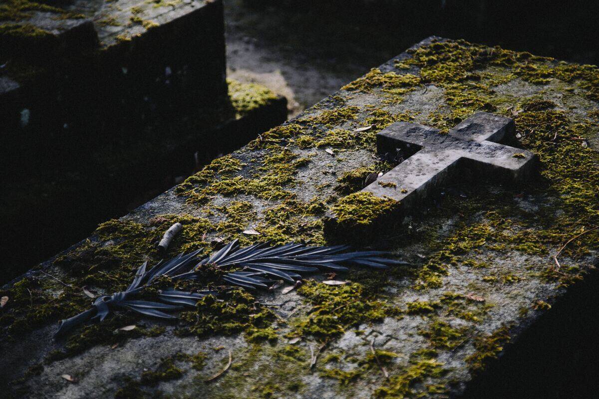 A headstone with a large cross on it, covered in moss.