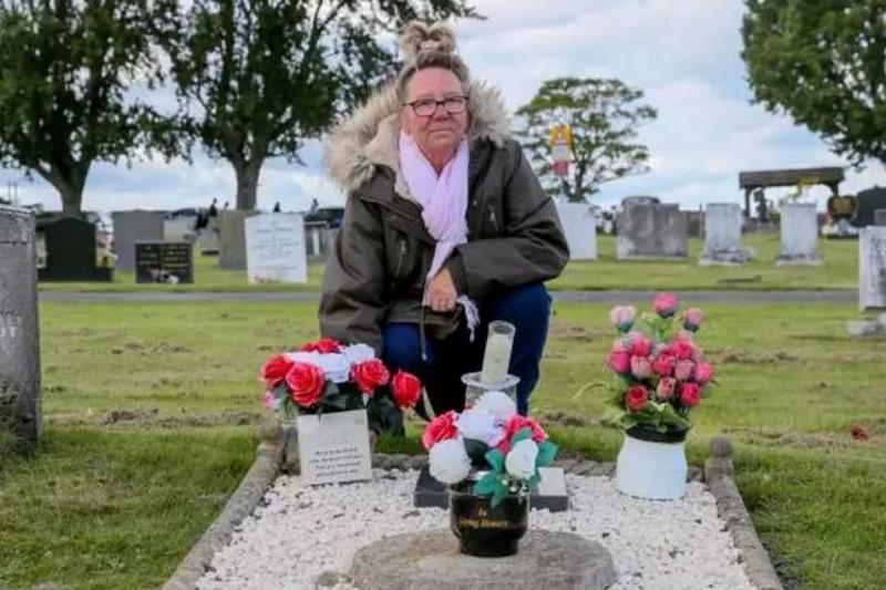 Ross kneeling at the now-properly labeled grave of her father, with candles and flowers placed on it.