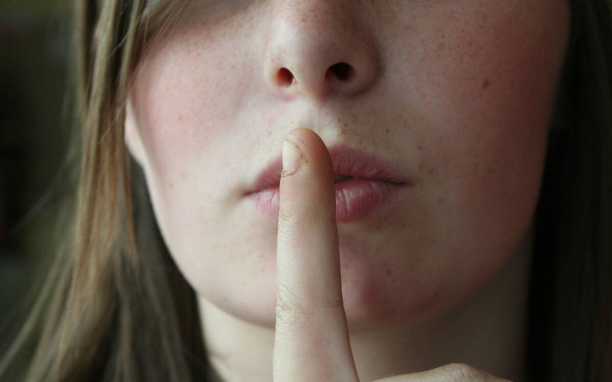 A woman holding a finger over her mouth in a 'shush' motion.