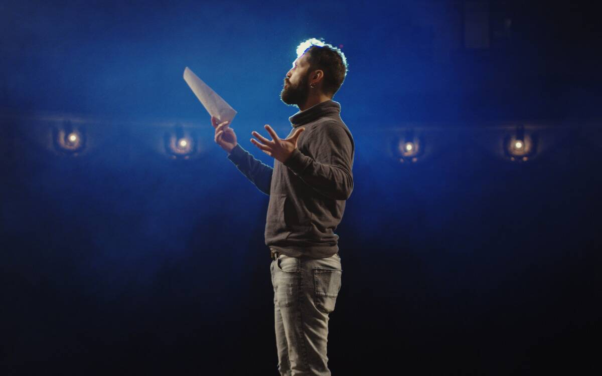 An actor standing on a stage reading off a script.