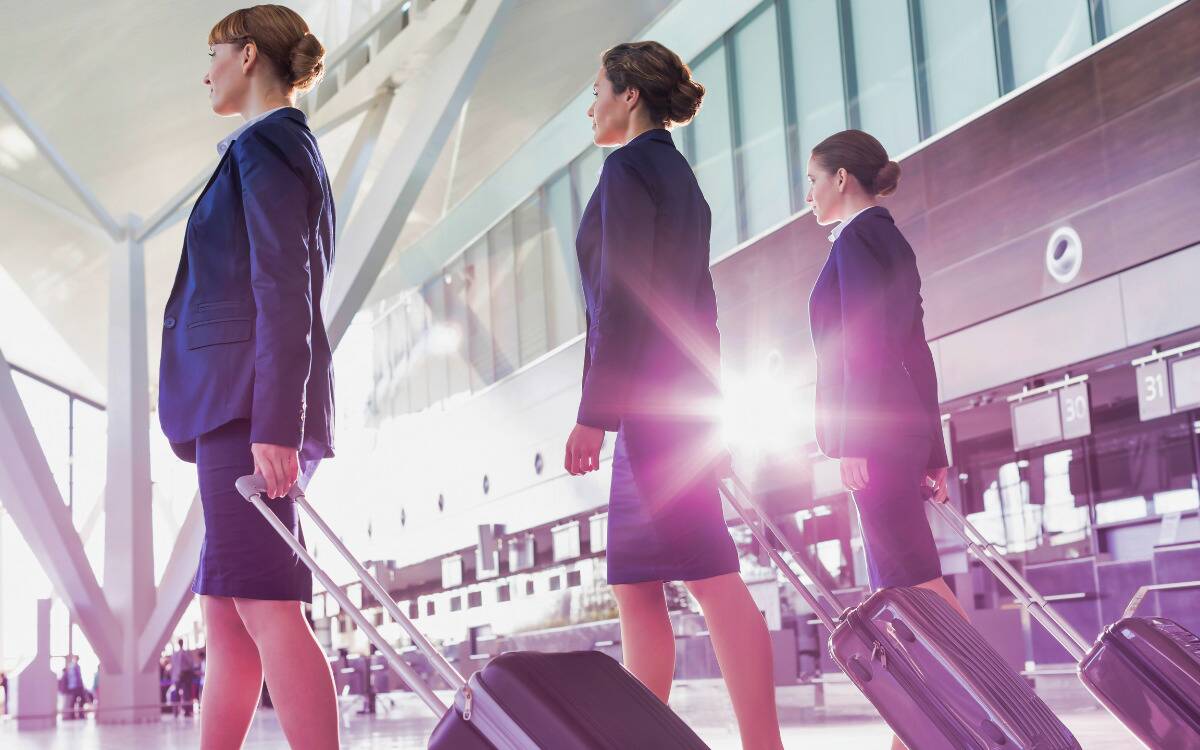 Three flight attendants walking through an airport toward their plane.
