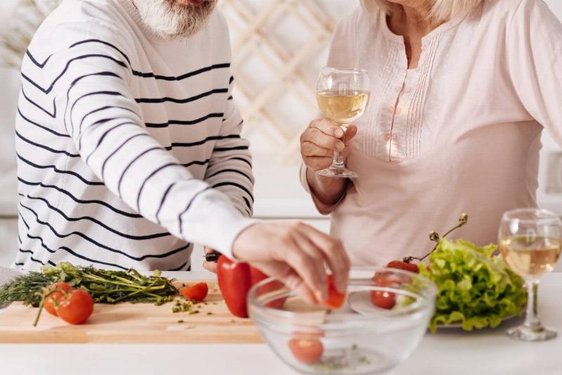A couple cooking dinner together while enjoying glasses of wine.