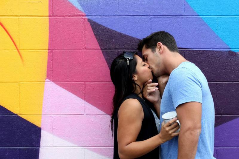 A couple kissing in front of a bright mural.