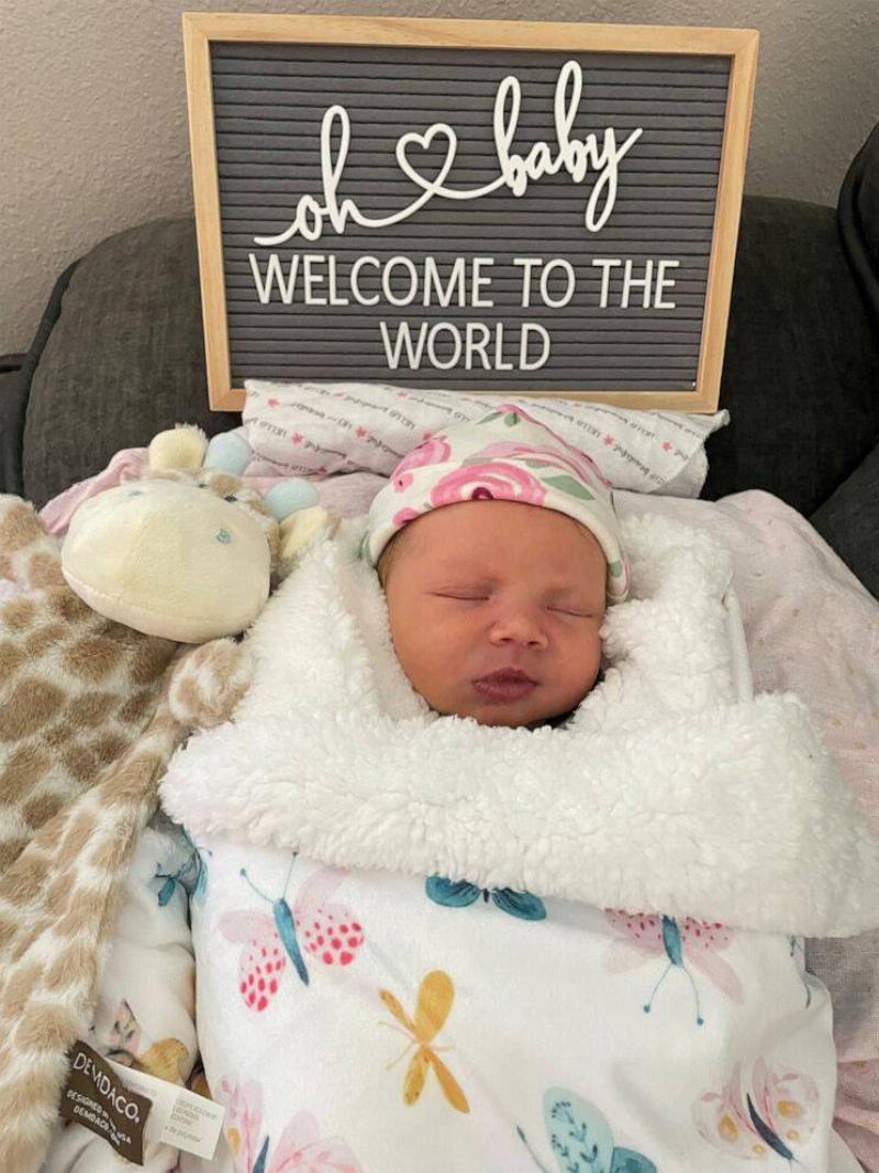 Zoey under a sign that reads 'Welcome To The World.'