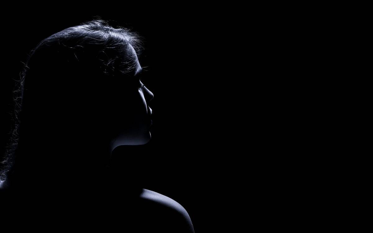 A dark photo of a woman looking to the side, her profile barely lit so we can just see her outline.