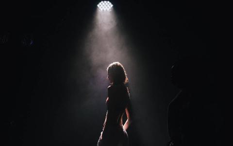 A woman on a dark stage lit only by a spotlight.