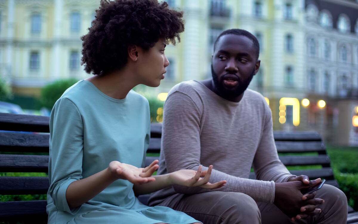 A couple arguing as they sit on a bench outside.