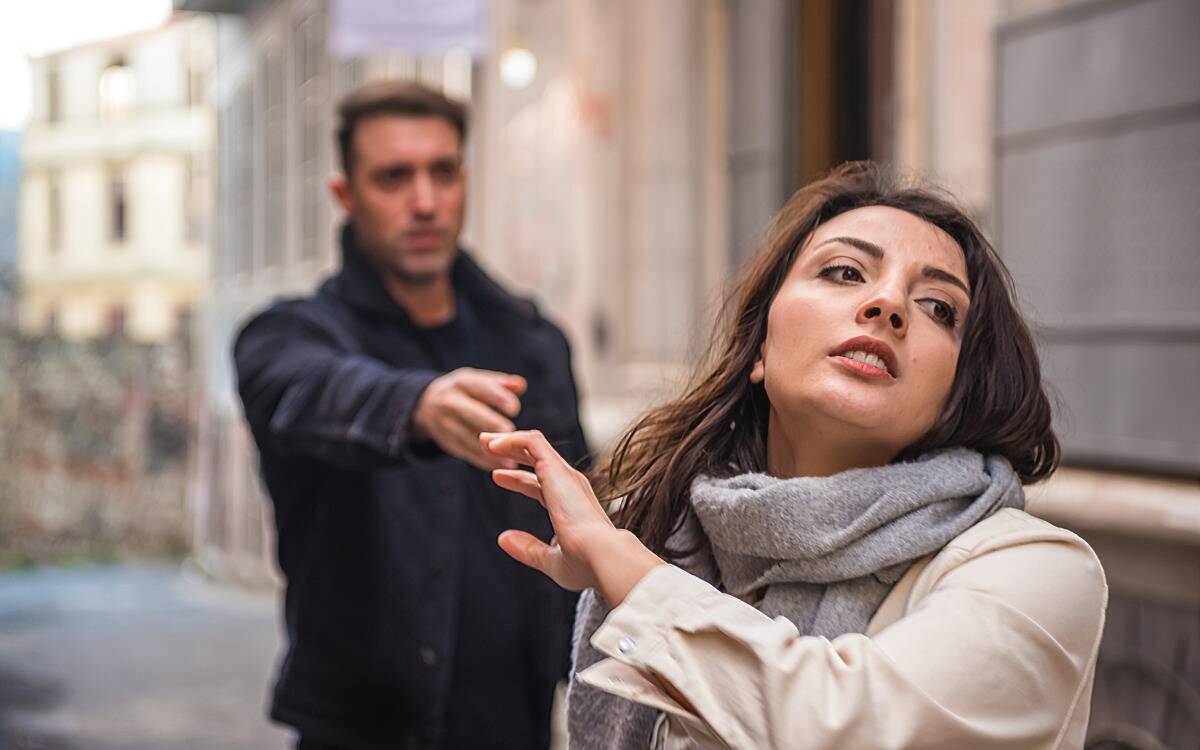 A woman walking away from a man, looking wistful, as he reaches for her hand.