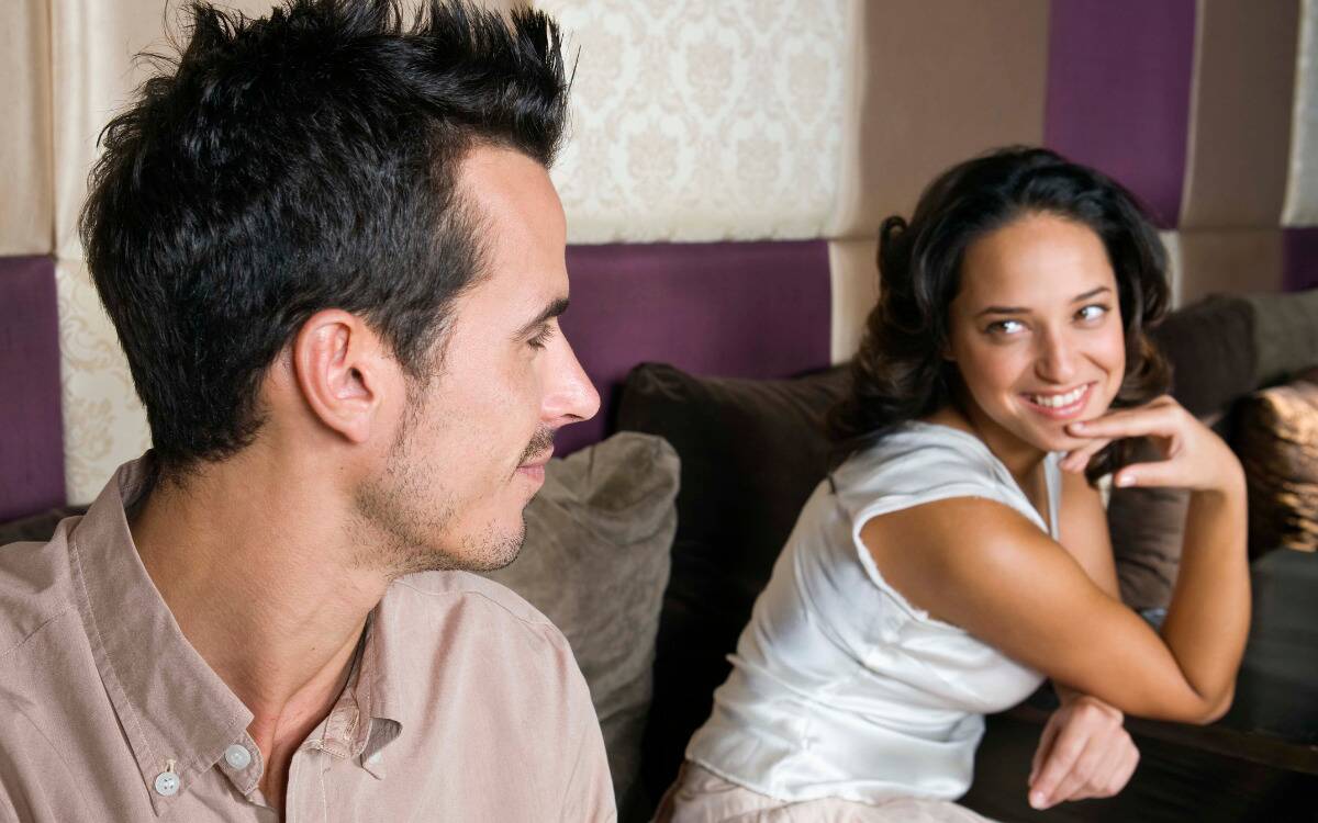 A man and a woman flirting at one another while sitting on a couch.