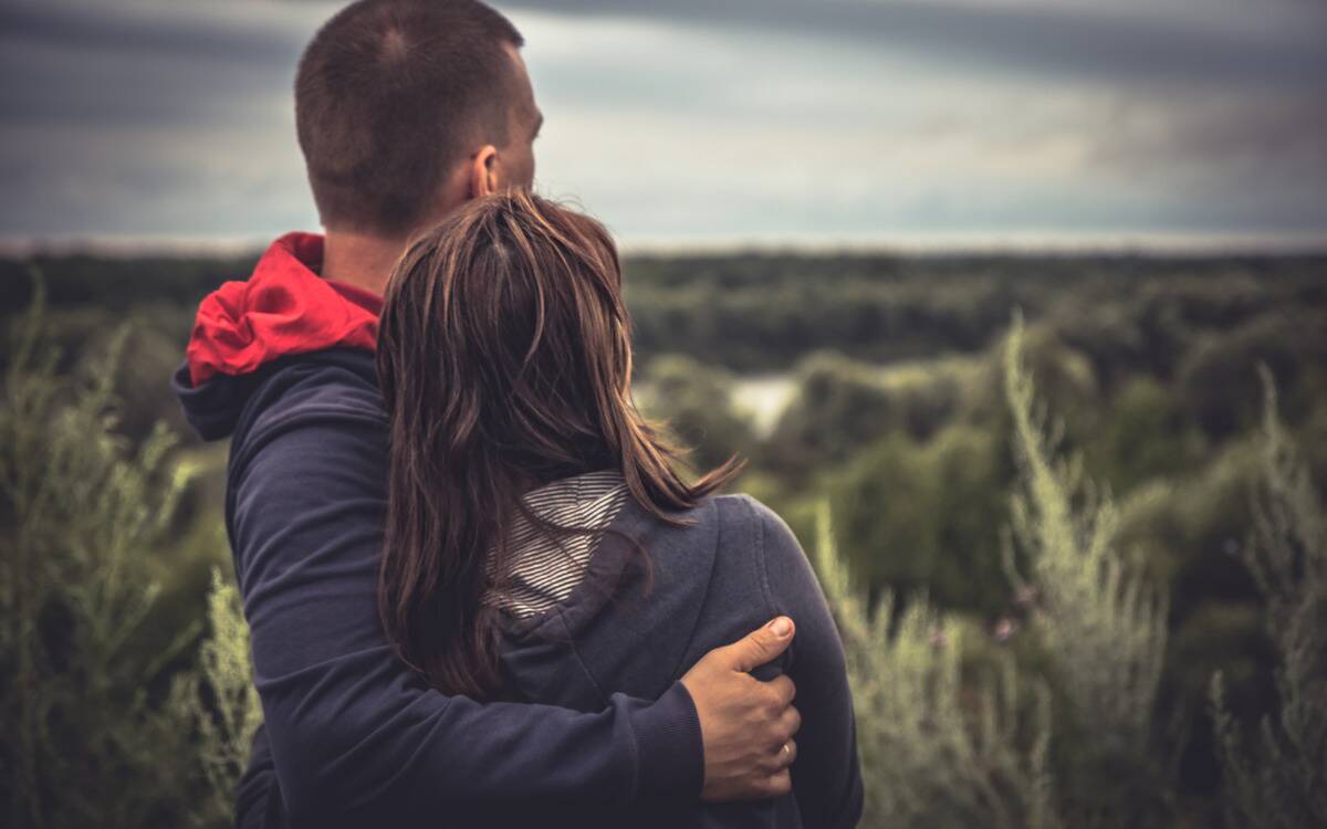 A couple looking out at a field, arms around one another.