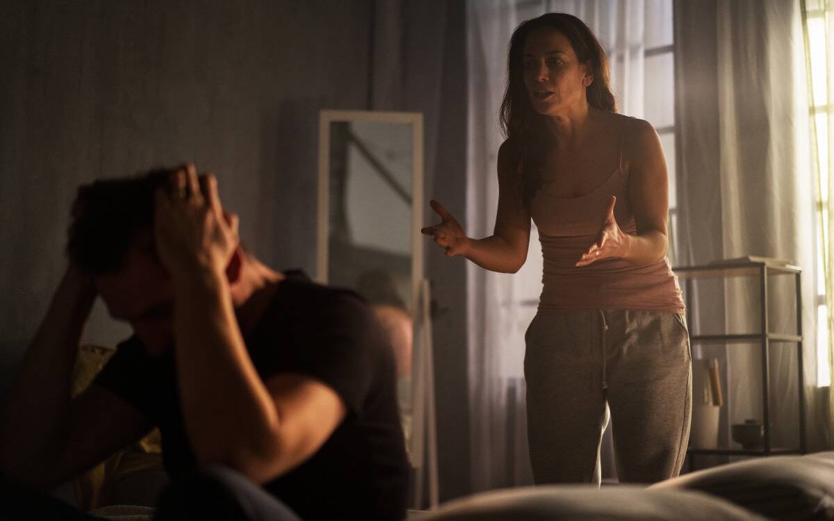 A woman yelling at a man sitting on the bed with his hands grabbing his head.