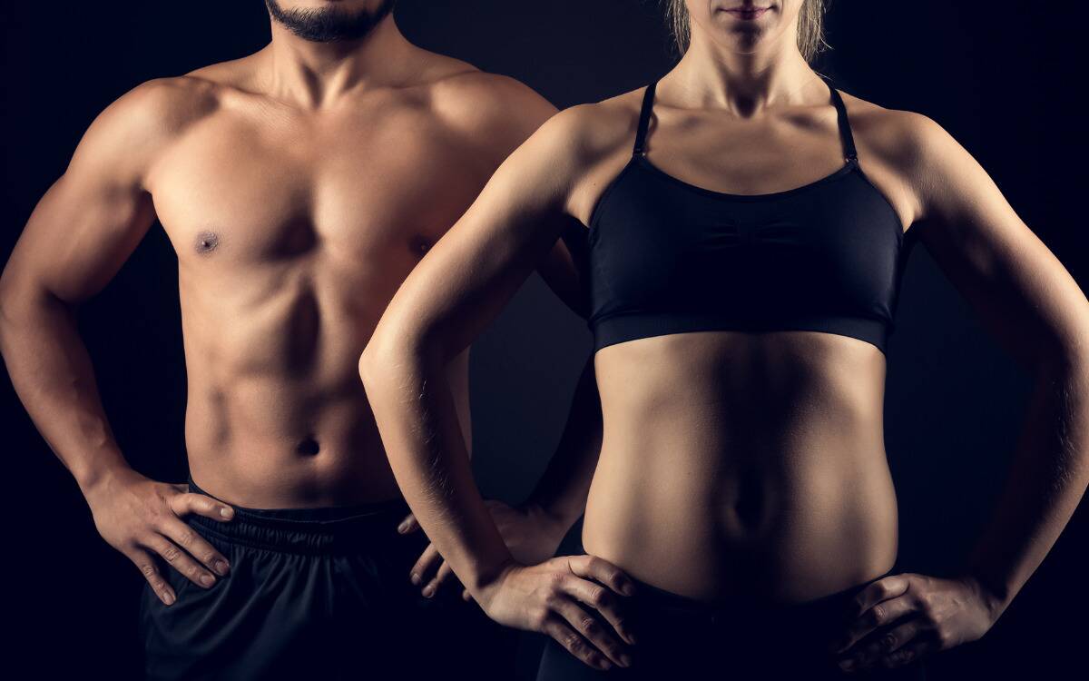 A muscular man and woman, the woman standing just in front of the man.