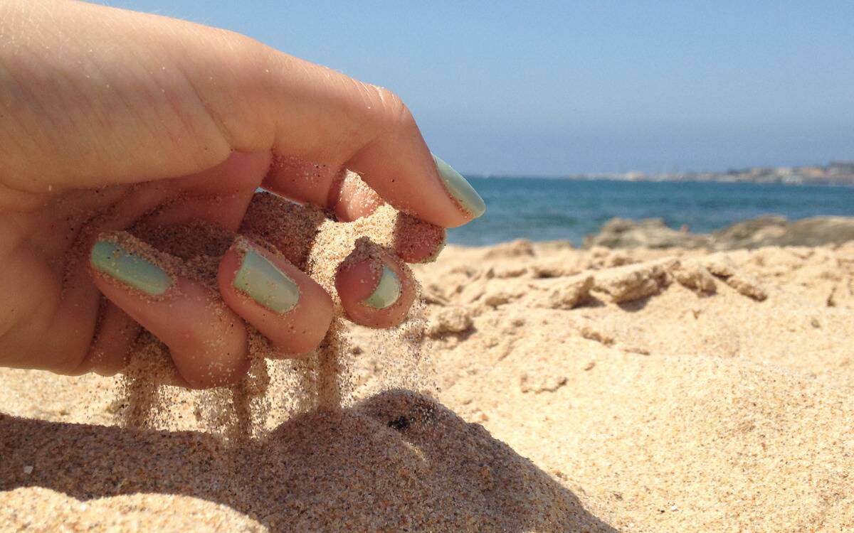 A closeup of someone's hand picking up sand, letting it run through their fingers.
