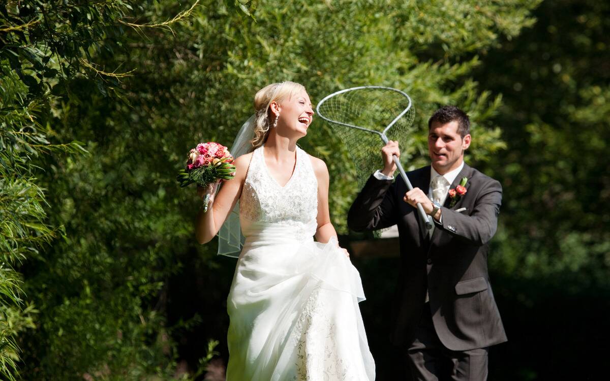 A man and woman on their wedding day, the man chasing the woman down with a large butterfly net.
