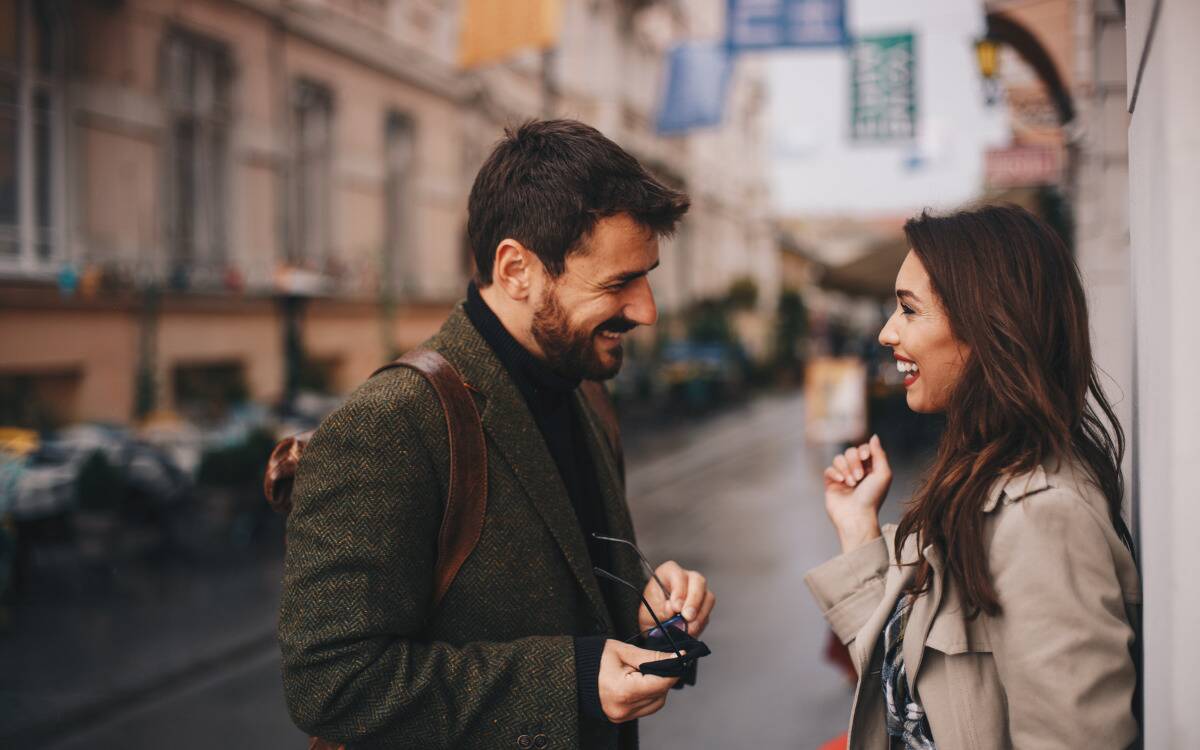 A man flirting with a woman on the street, the two smiling.
