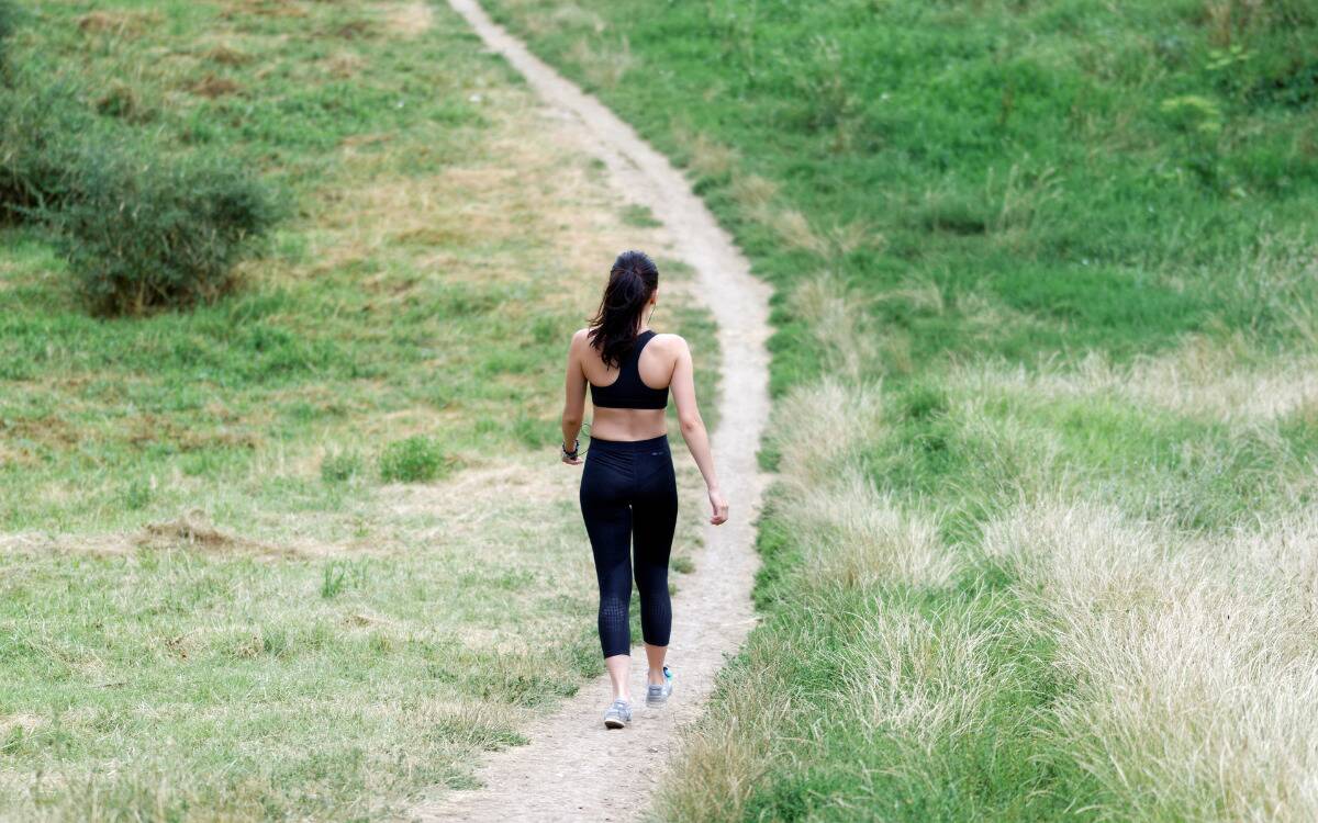 A woman walking down a path made in grass, wearing workout gear.