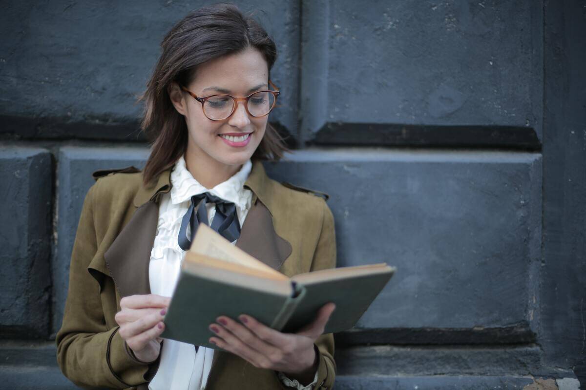 A woman smiling as she reads a book outside.