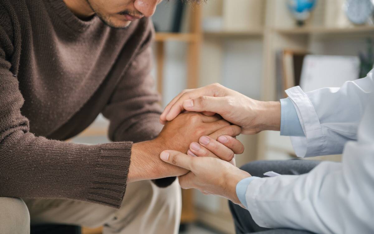 A man being comforted by someone else holding his clasped hands.