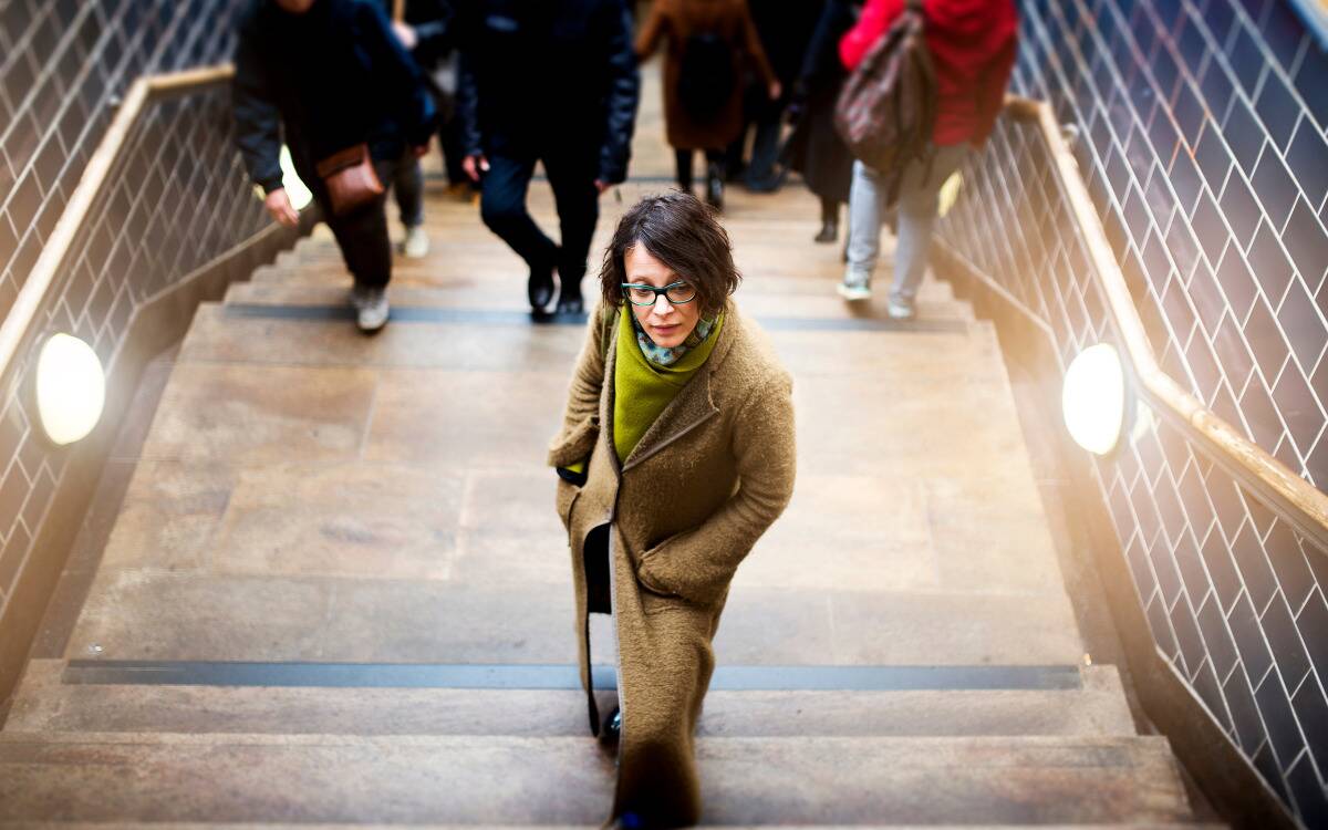 A woman standing on a set of stairs, ahead of the crowd, looking confident.