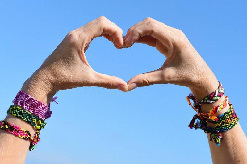 Someone making a heart shape with their hands, colorful beaded bracelets on both arms.