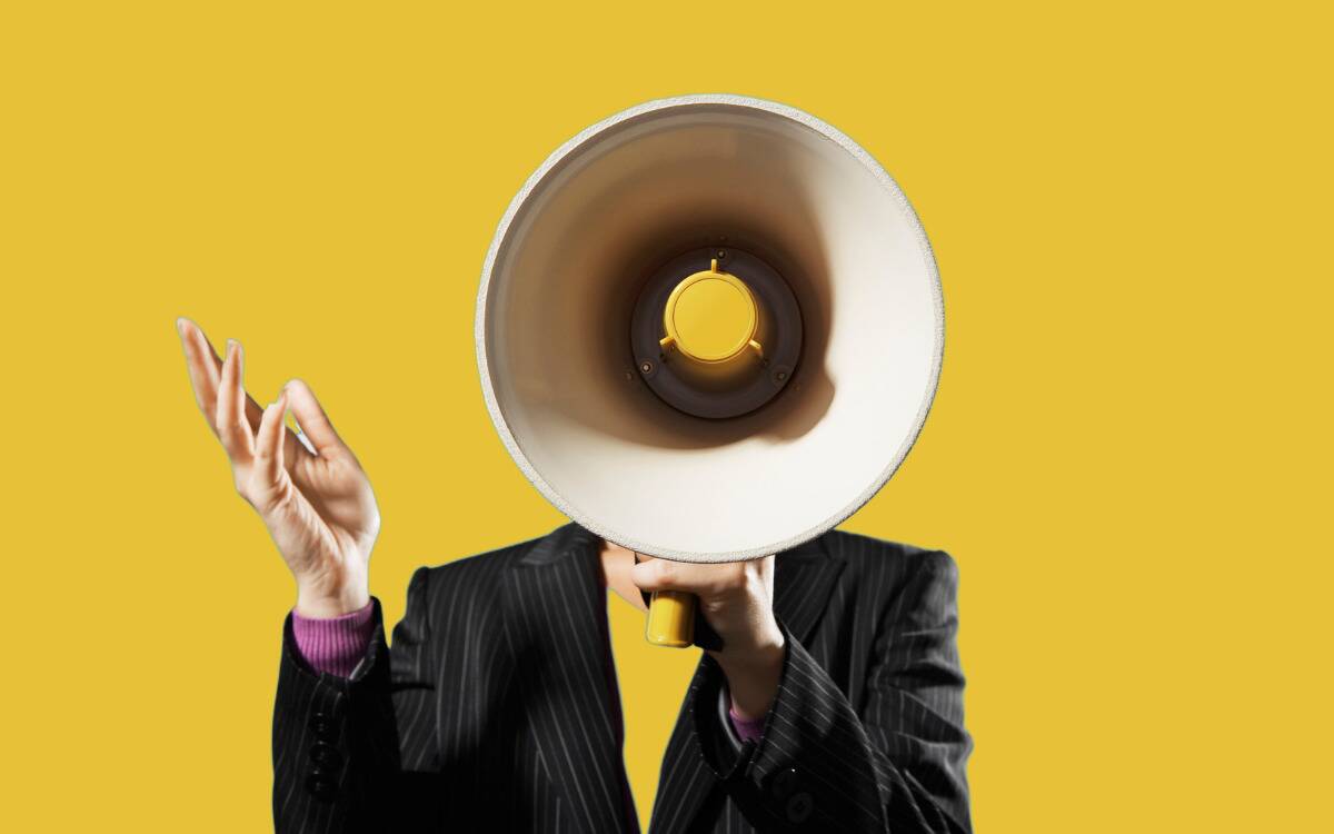 Someone in a suit against a yellow background holding up a megaphone so it perfectly covers their head.