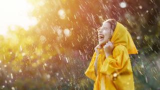 A child in a yellow rain jacket  laughing during a sunshower.