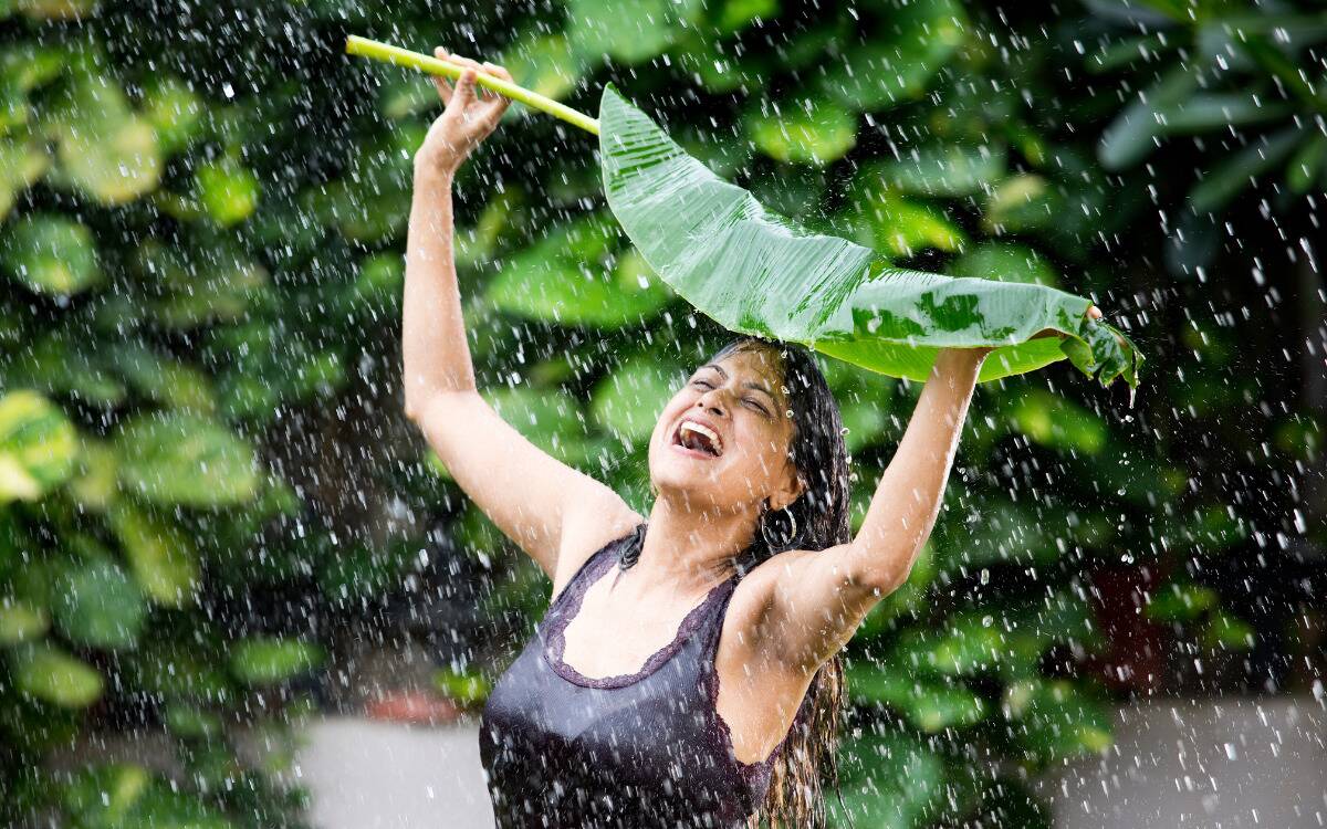 A woman holding a large leaf over her head to protect herself from the rain.