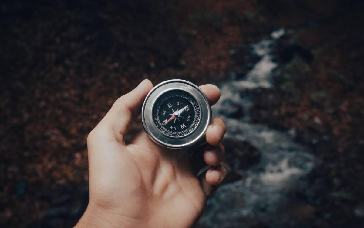 Someone holding a compass up in front of a creek they're walking next to.