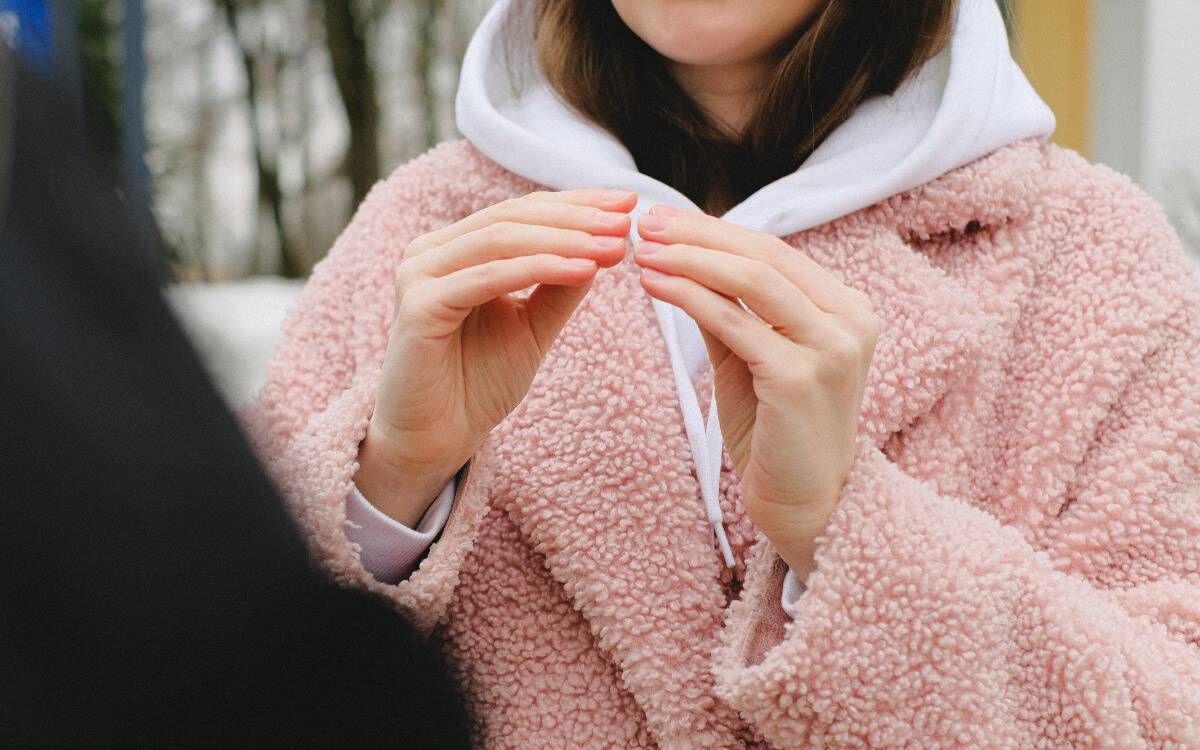 A woman in a fuzzy pink jacket speaking with her hands.
