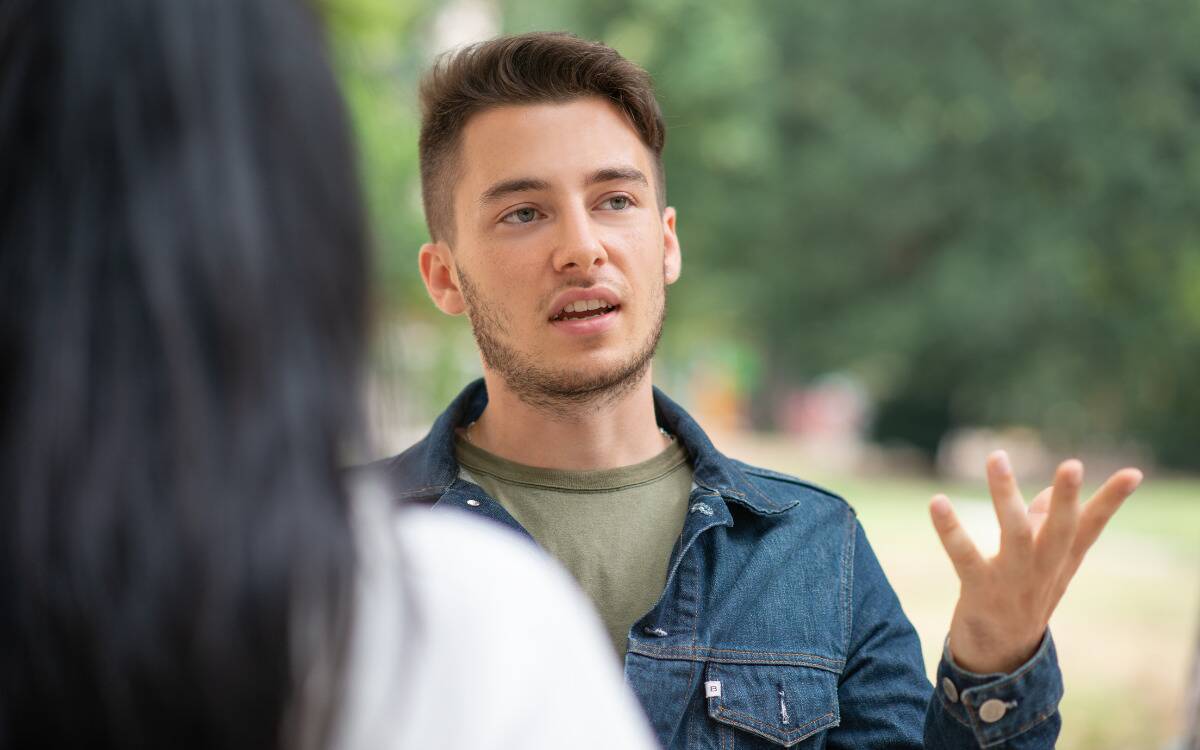 A man speaking to a friend, gesturing with his hand.