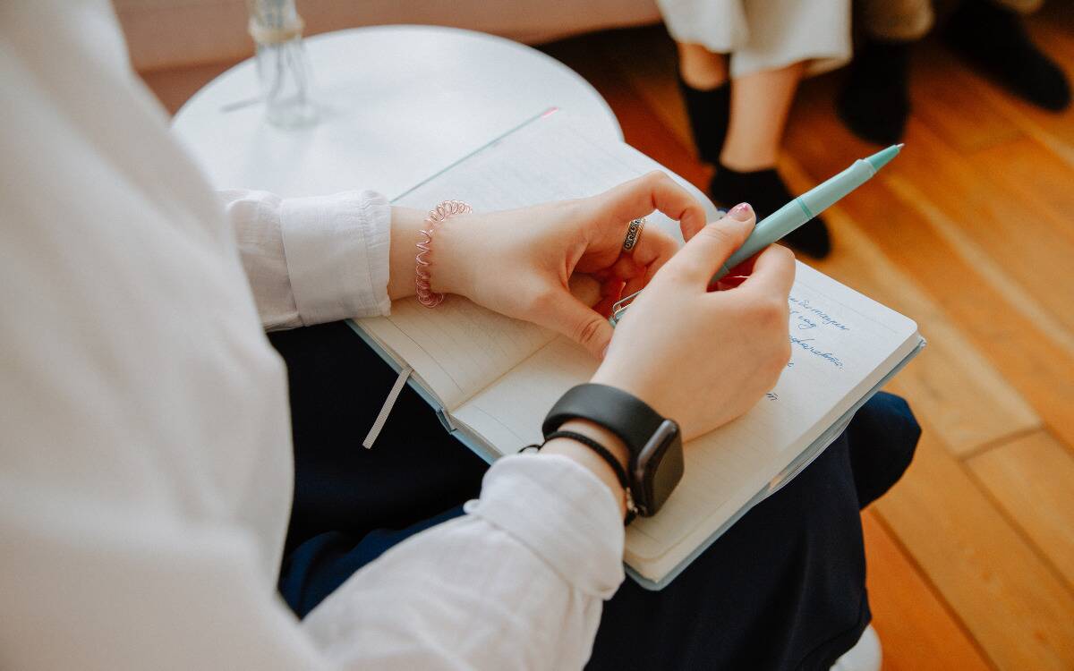 Someone holding a journal and a pen with thoughts written down inside.