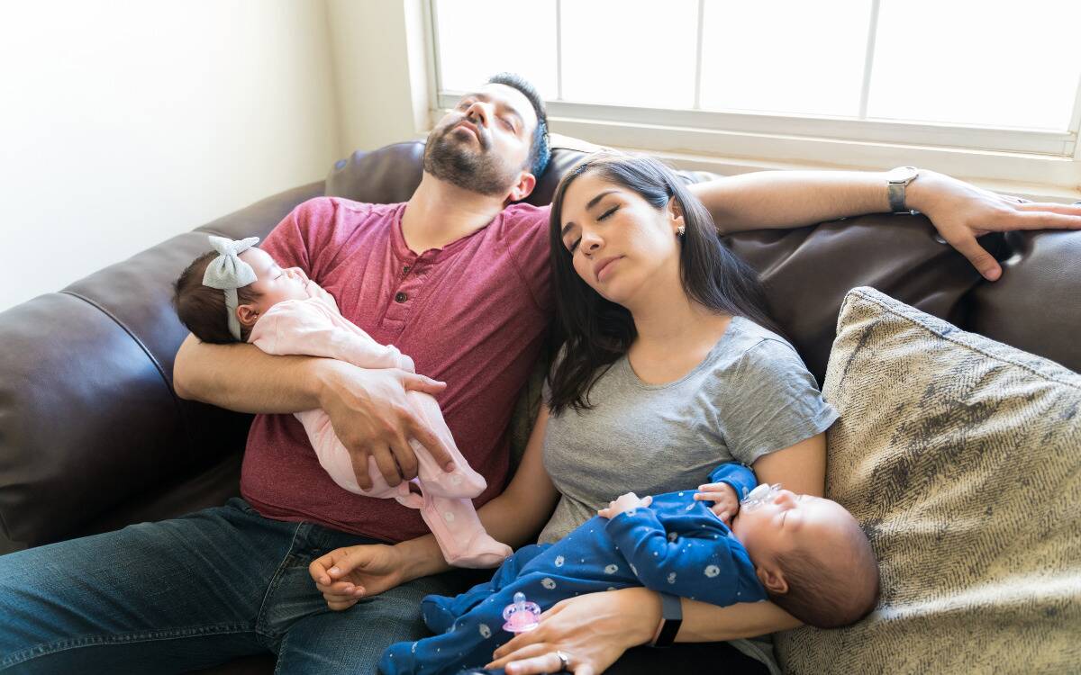 Two parents sleeping as they hold their babies, who are also sleeping.