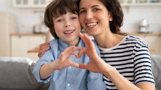 A mom making half a heart shape with her hand, her son making the other half.