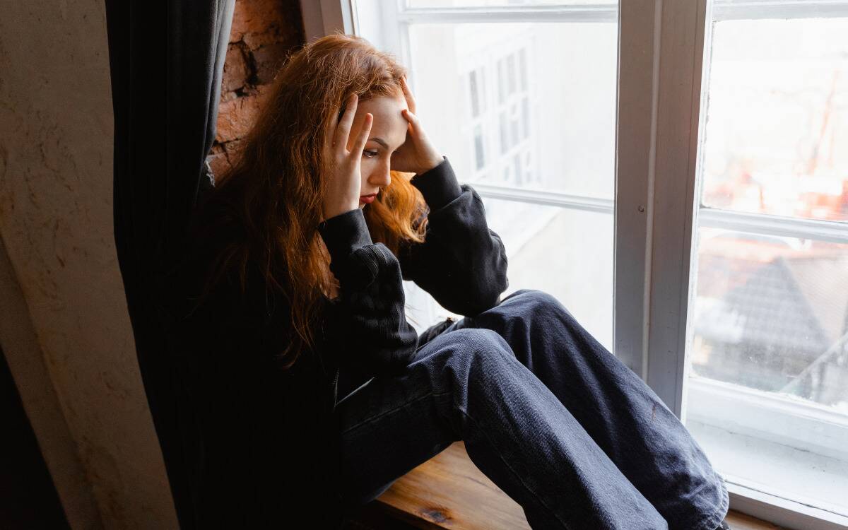 A woman sitting on a windowsill, head in her hands.