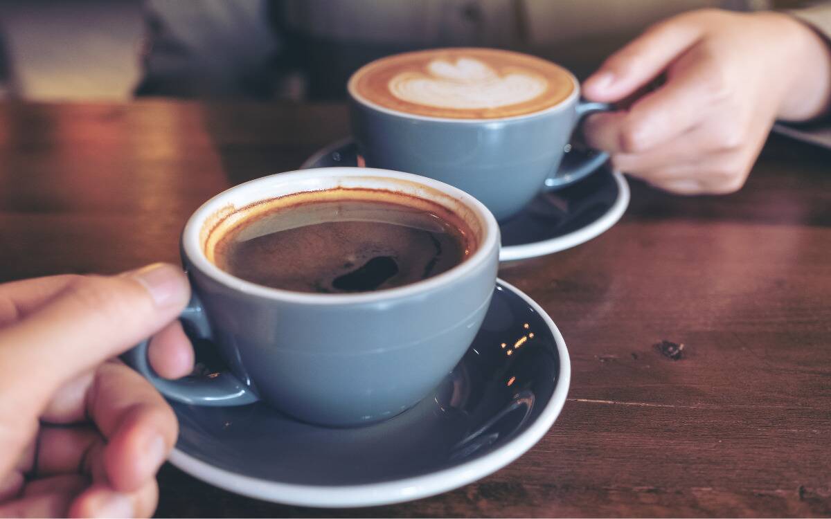Two cups of coffee on a table, each being held by their handle.