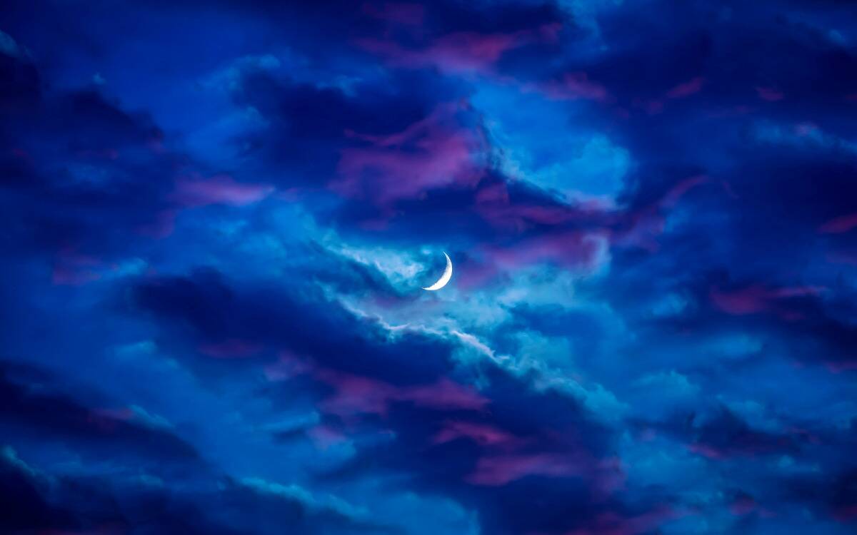 The new moon in the center of the sky, amidst blue and purple clouds.