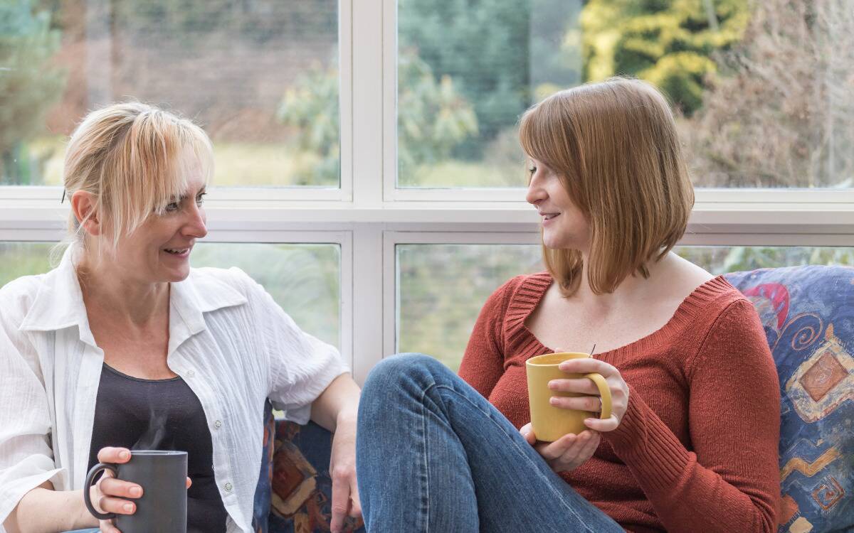 Two women having an amicable conversation, both holding mugs.