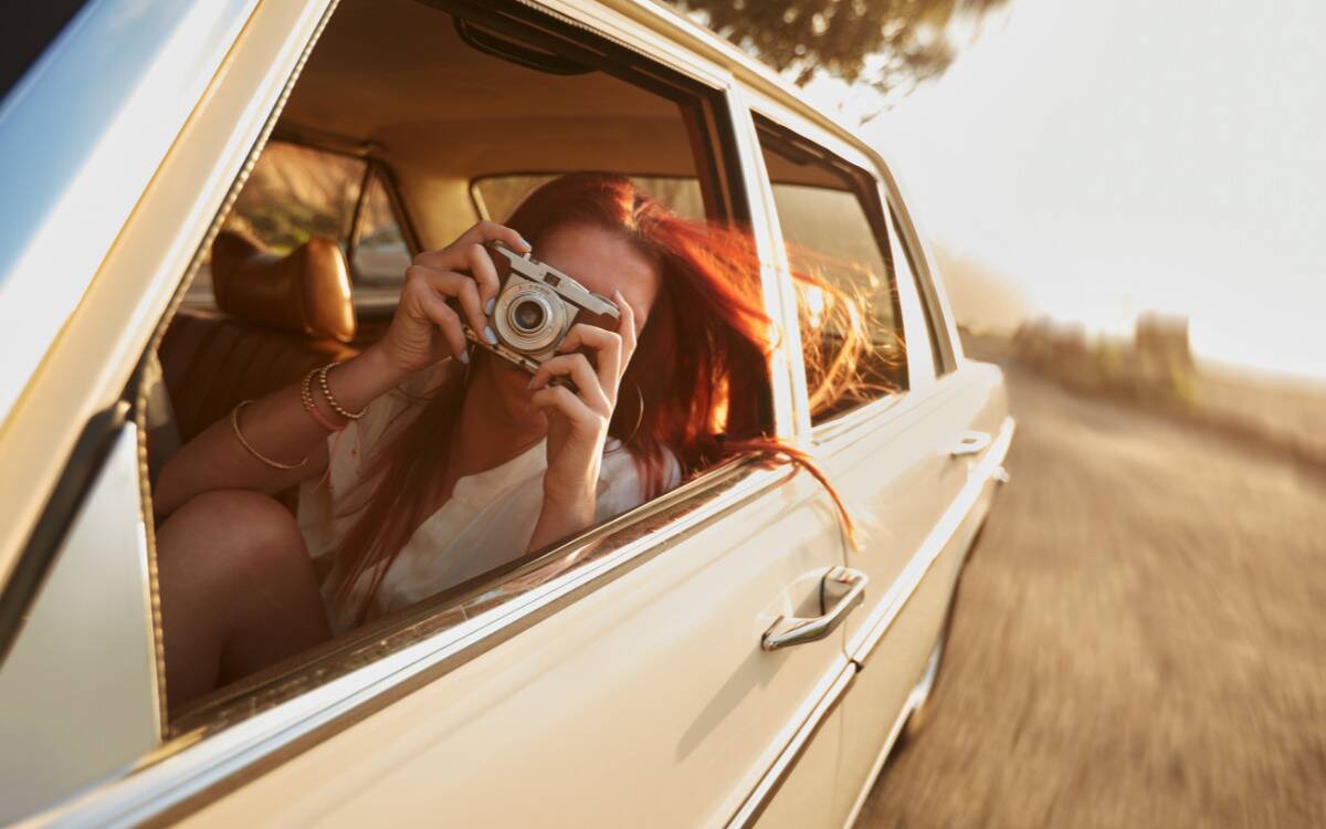 A woman taking a photo out a car window.