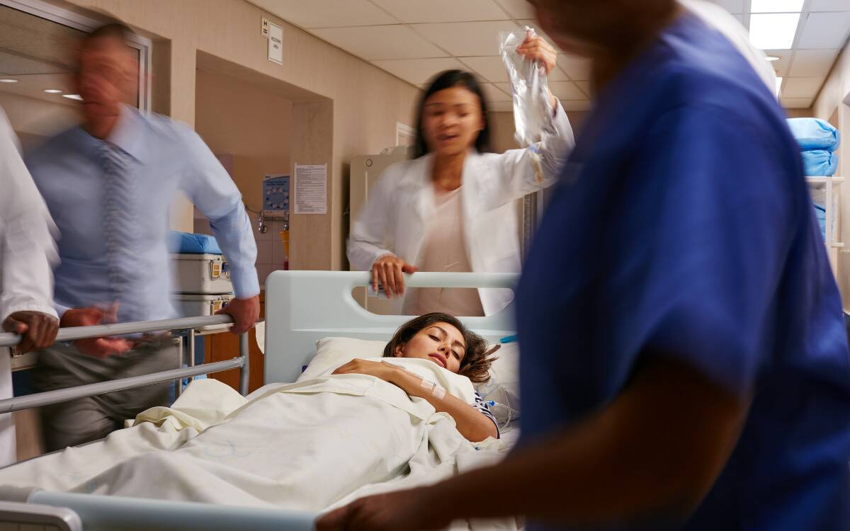 A group of doctors and nurses rushing a woman in a hospital bed down a hallway.